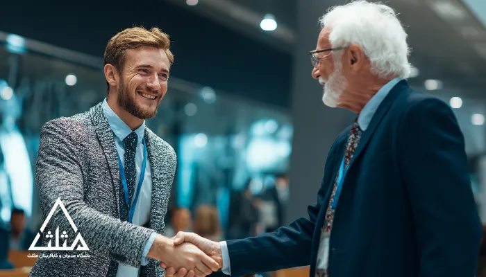 تصویر دست‌دادن یک مدیر جوان با یک مدیر باتجربه در رویدادی حرفه‌ای؛ نمادی از نقش باشگاه مدیران در ایجاد پیوند میان رهبران جوان و مدیران باتجربه برای انتقال تجربه، mentorship و رشد حرفه‌ای.