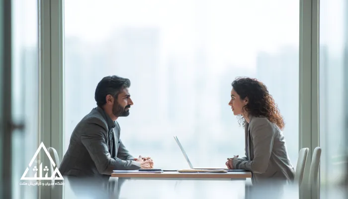 دو مدیر (یک مرد و یک زن) روبه‌روی هم در جلسه مذاکره سازمانی، با گفت‌وگوی متمرکز و آرام کنار لپ‌تاپ؛ تصویر نماد مذاکره حرفه‌ای و رسیدن به توافق بدون تنش.