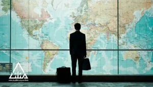 مدیر کت‌وشلواری از پشت، مقابل نقشه بزرگ جهان در سالن ترانزیت ایستاده و چمدان و کیف دستی کنار اوست؛ نمادی از سفر به‌عنوان ابزار یادگیری و گسترش نگاه مدیریتی.